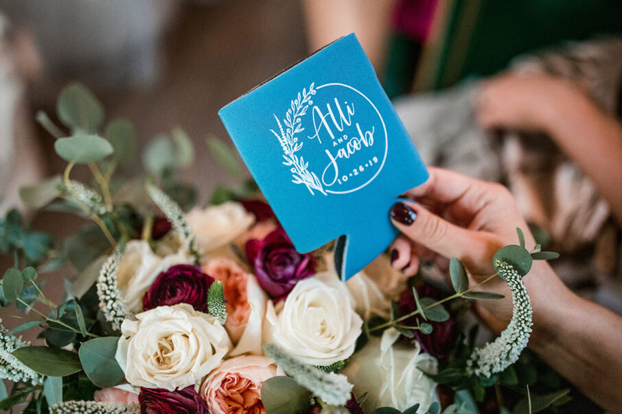 Someone holds a custom wedding koozie with the bride and groom's names