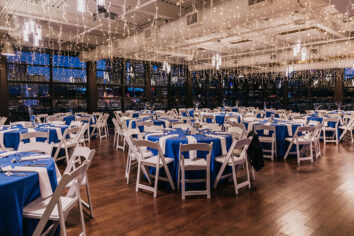 A corporate reception in the Dyer space filled with hanging fairy lights and round tables with bright blue linens and white chairs