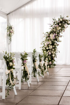 Ceremony Setup on Rooftop with White Drapery and White Seating with Floral Arrangements of Purple and Green