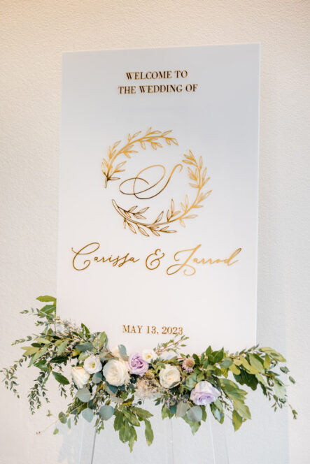Carissa and Jarrod's White Wedding Welcome Sign with Gold Lettering and Floral Arrangement