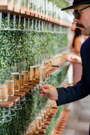 Guest grabbing champagne from greenery wall during reception