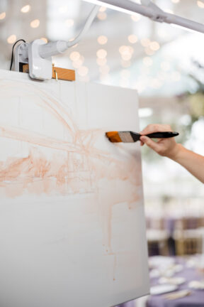 A close-up image of a live wedding painter with her brush to the canvas as she captures the scene