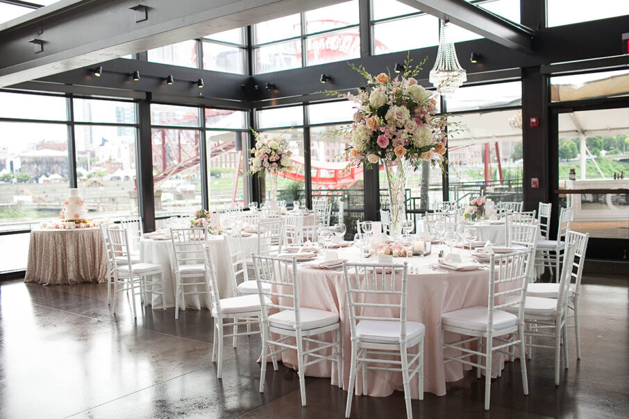 Glam pink wedding reception setup with pale pink table linens, white chairs, and large elevated floral centerpieces in class vases at The Bridge Building, downtown Nashville wedding venue