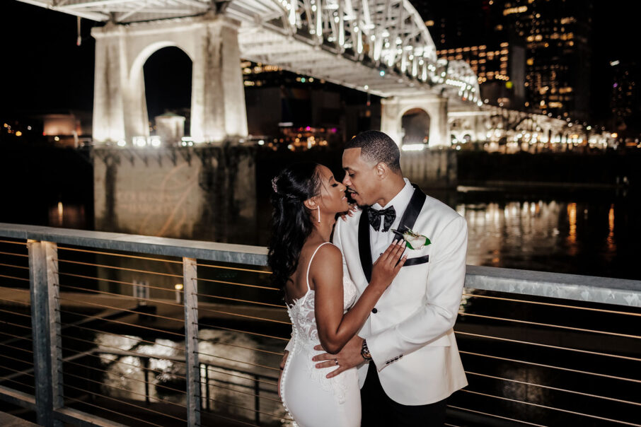 Bride and groom pose along riverfront patio
