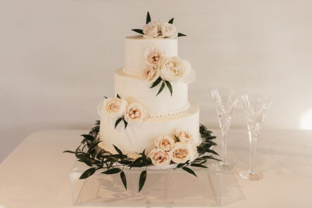 A classic white wedding cake with rose decor and greenery for classic romantic wedding at The Bridge Building, downtown Nashville wedding venue