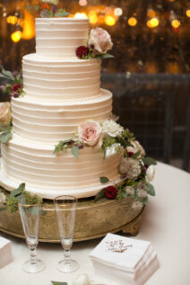 Four-tier white textured wedding cake with red and pink rose decor for romantic winter wedding at The Bridge Building, downtown Nashville wedding venue