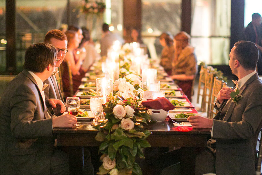 Guests seated at wedding reception head table with magnolia leaves for table runner and red napkins for romantic winter wedding at The Bridge Building, downtown Nashville wedding venue