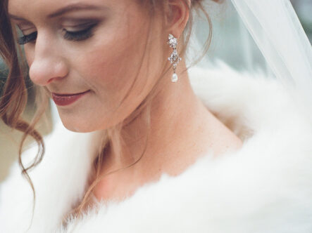 Close-up of bride's face with dangling pearl earrings and white fur shawl for romantic winter wedding at The Bridge Building, downtown Nashville wedding venue