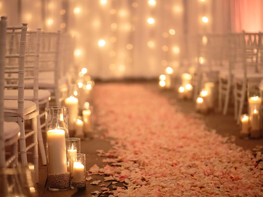 A close-up of pink rose petals creating an aisle to the altar, surrounded by candle aisle markers for rose gold New Year's Eve wedding at the Bridge Building, a downtown Nashville wedding venue