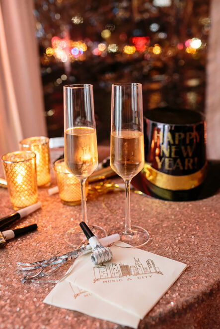 Bride and groom champagne flutes set up on rose gold sequin table linens with happy new year's hat and streamers for New Year's Eve wedding at the Bridge Building, a downtown Nashville wedding venue