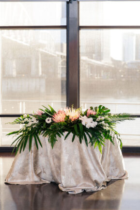 Sweetheart table for indoor wedding reception with large tropical leaves and pink protea for tropical-inspired wedding at the Bridge Building, a downtown Nashville wedding venue