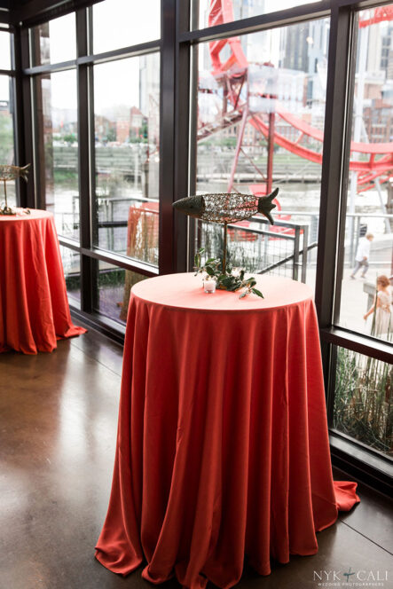 Cocktail tables with red linens and metal fish art centerpiece for nautical themed rehearsal dinner