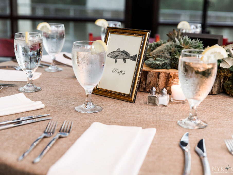 Table decor with fish-themed table numbers, succulents, and slice of wood tree centerpiece for nautical themed rehearsal dinner