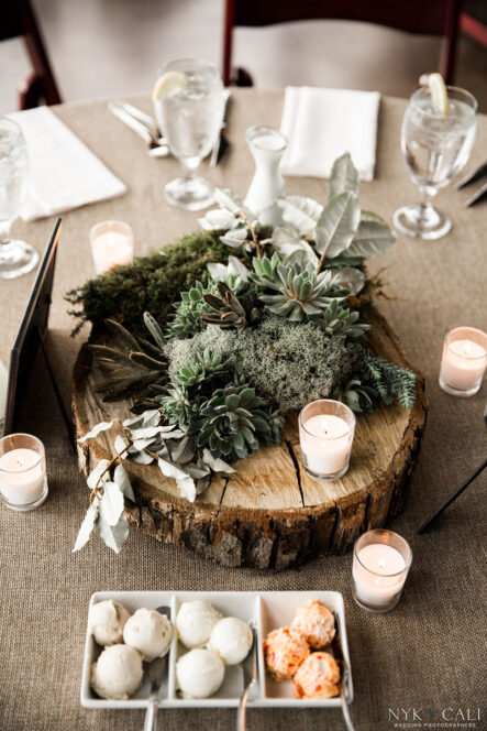 Table decor centerpiece with succulents, moss, and small votive candles on a slice of wooden tree for nautical themed rehearsal dinner