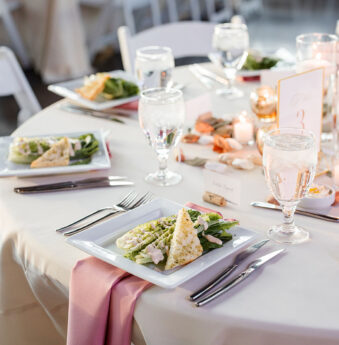 A wedding table place setting with a preset plated salad on a rose pink napkin on ivory table linens