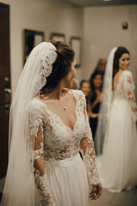 Bride in long sleeve lace wedding dress looks over the shoulder at herself in full-length mirror at the Bridge Building, a downtown Nashville wedding venue
